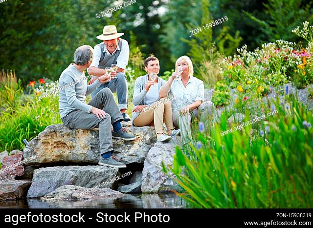 Zufriedene Senioren sitzen mit einem Glas Weißwein im Sommer im Garten