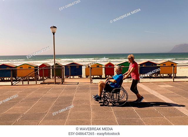 Side view of senior man being pushed on wheelchair by senior woman