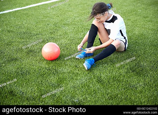 UK, Female soccer player tying shoe in field
