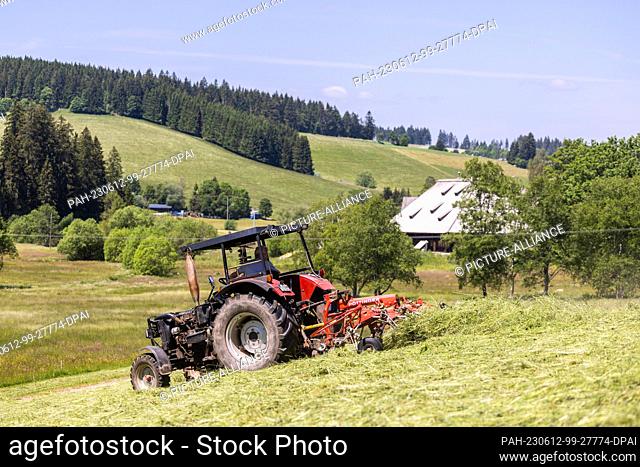 12 June 2023, Baden-Württemberg, Schönwald im Schwarzwald: A farmer drives a tractor over a previously mowed meadow, turning the grass to make hay