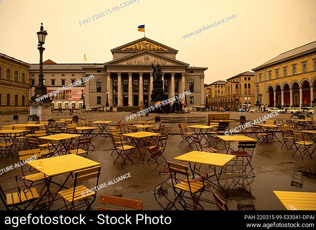 15 March 2022, Bavaria, Munich: Over the Max-Joseph-Platz and the Staatsoper bad weather with Sahara dust is coming up that colors the sky yellow/orange