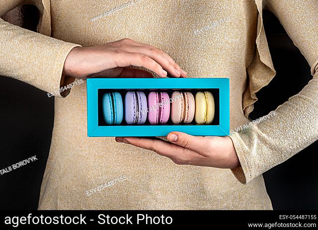 Female hands holding multicolored macaroons in gift box