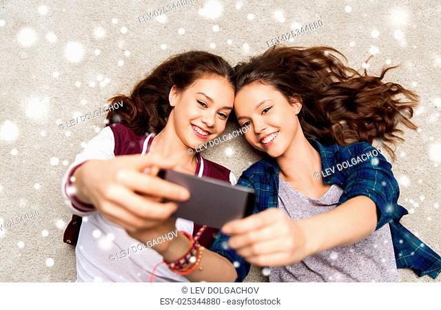 people, technology, winter, christmas and friendship concept - happy smiling pretty teenage girls or friends lying on floor and taking selfie with smartphone...