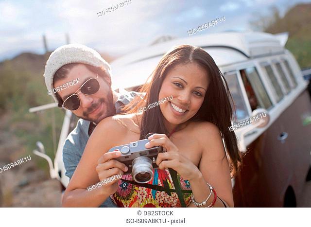 Young woman holding camera with boyfriend on road trip, smiling