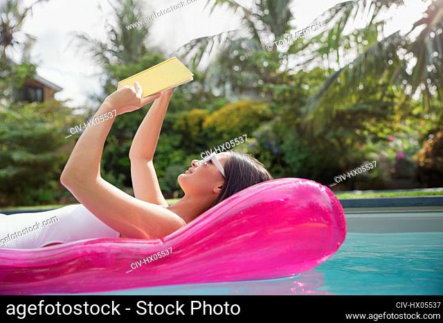 Woman reading book on inflatable raft in sunny summer swimming pool