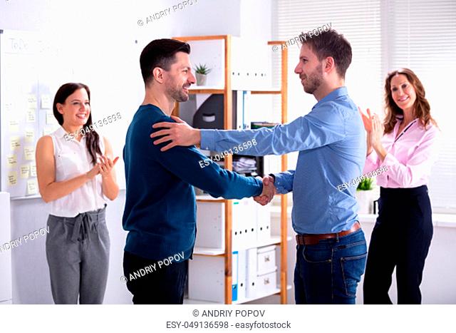 Two Happy Partners Shaking Hands While Other Colleagues Clapping In Office