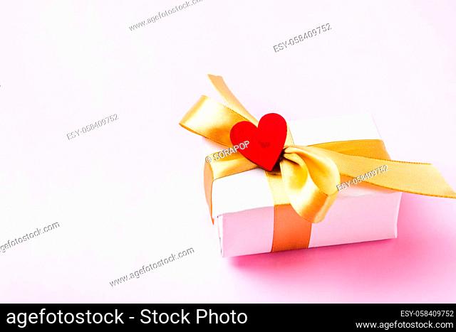 Valentines' day background concept. White gift box with a golden bow ribbon and wood red hearts composition greeting card for happy love isolated on pink...
