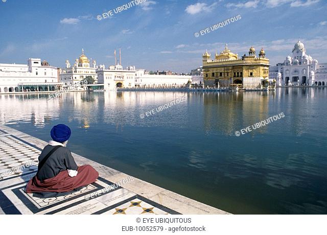 Sikh man sitting on marble walkway beside the sacred pool surrounding the Golden temple