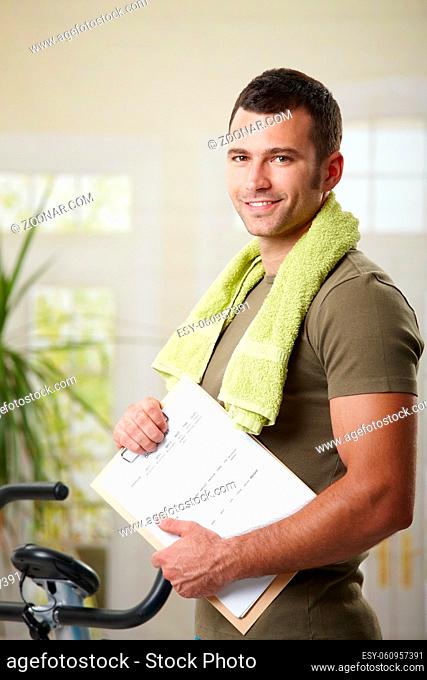 Man wearing sportswear standing in living room at home, holding training plan