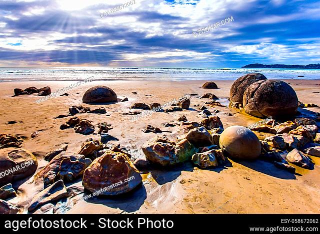 The popular tourist attraction. The huge round stone boulders Moeraki and their remains on sandy beach. New Zealand. Low tide in the Pacific ocean
