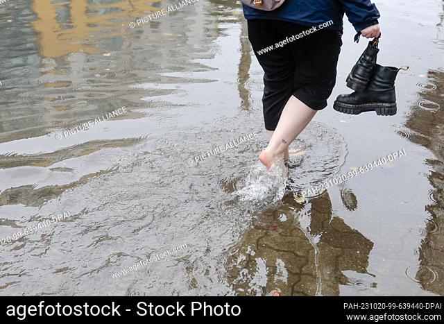 20 October 2023, Schleswig-Holstein, Flensburg: A woman walks barefoot through the water in the city center. A powerful storm pushes the Baltic Sea water ashore...