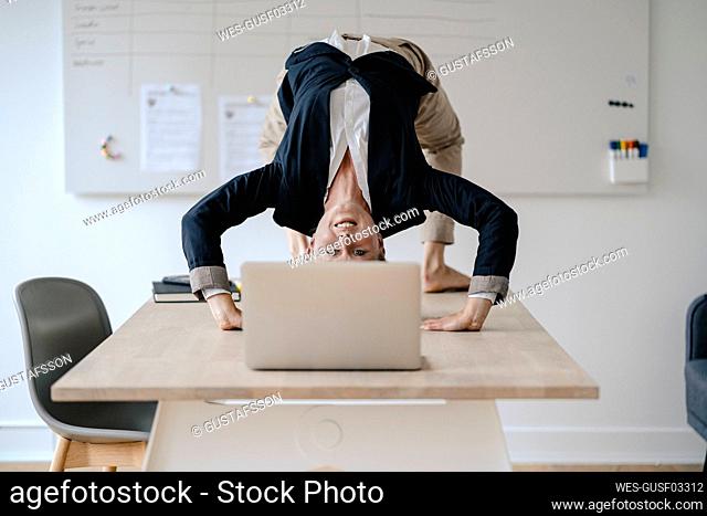 Young businesswoman practicing yoga on desk in office