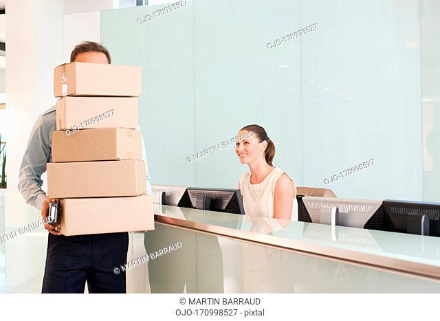 Delivery man holding stack of boxes in reception area