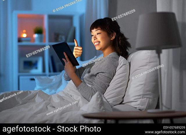 woman with tablet pc in bed has video call at night