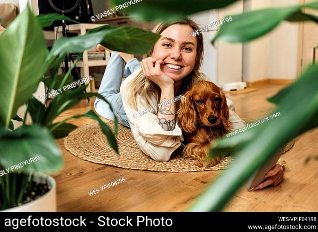 Smiling woman with dog lying in living room at home