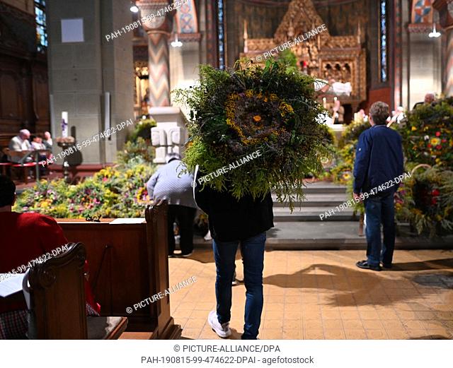 15 August 2019, Baden-Wuerttemberg, Gengenbach: A man carries a huge bouquet of herbs in front of the altar of the city church