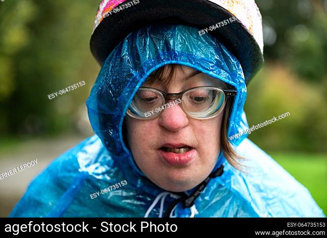 Close up portrait of a 41 yo woman with Down Syndrome, wearing a bike helmet and a blue rain poncho, Tienen, Flanders, Belgium