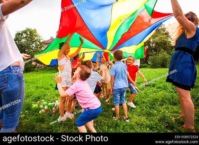 Kids hide under rainbow parachute, outdoors game at summer camp