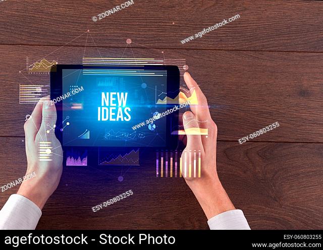 Close-up of hands holding tablet with NEW IDEAS inscription, modern business concept