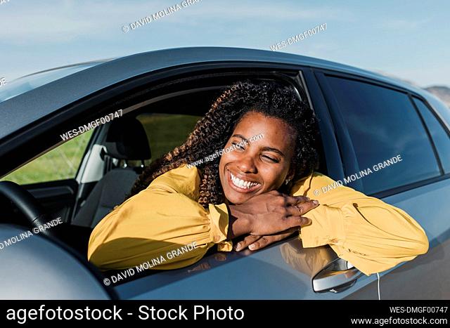 Happy woman leaning out of car's window on sunny day