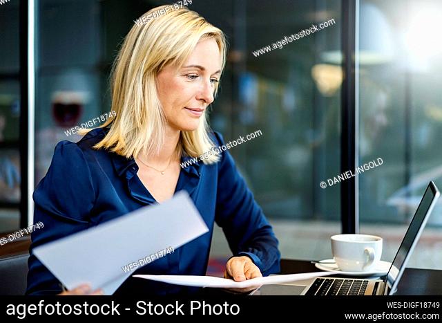 Smiling businesswoman with documents looking at laptop