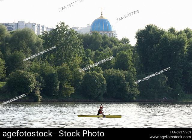 RUSSIA, MOSCOW - MAY 18, 2023: A man paddles a boat on Moscow's Borisovo Ponds. Pictured: the Church of the Holy Trinity at the Borisovo Ponds (background)