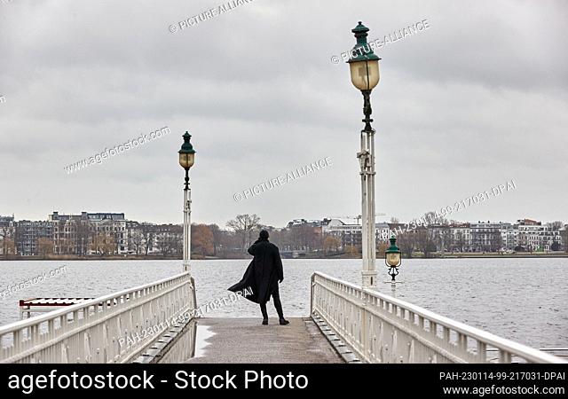14 January 2023, Hamburg: A man in a black coat stands on the bridge at the Rabenstraße jetty on the Outer Alster and looks out over the water while the wind...