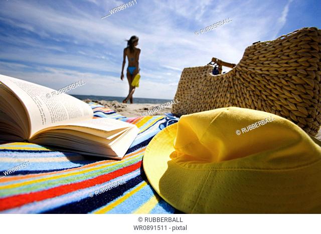 Beach towel with book and bag with a young woman in background