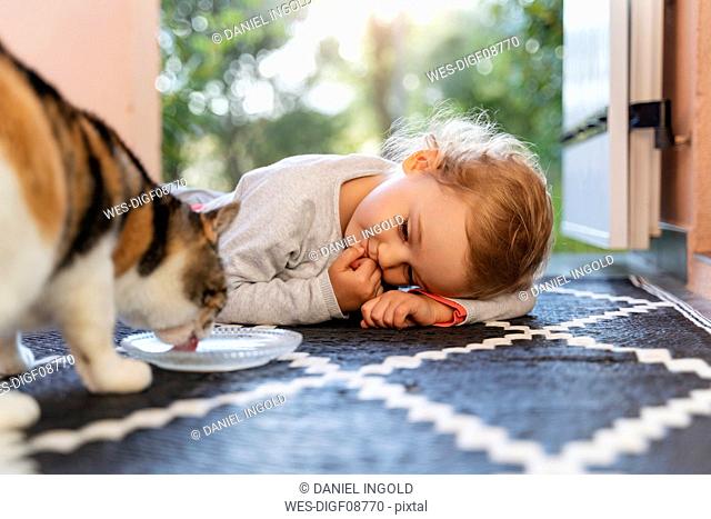 Cute toddler girl watching cat drinking from bowl