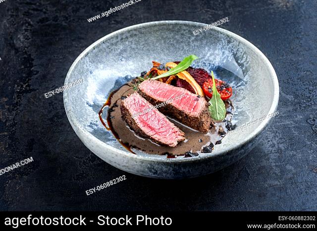 Modern Style Italian tagliata di manzo with dry aged sliced sirloin steak and tried vegetable in truffle sauce served as close-up in a design ceramic bowl with...