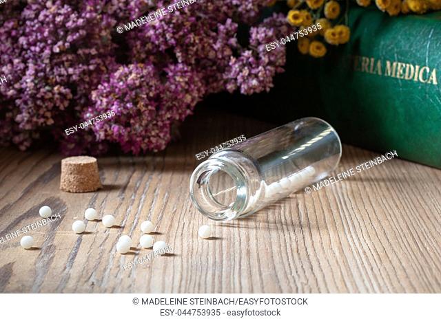 A bottle of homeopathic globules with dried herbs and a materia medica, i. e. a list of remedies and their therapeutic properties