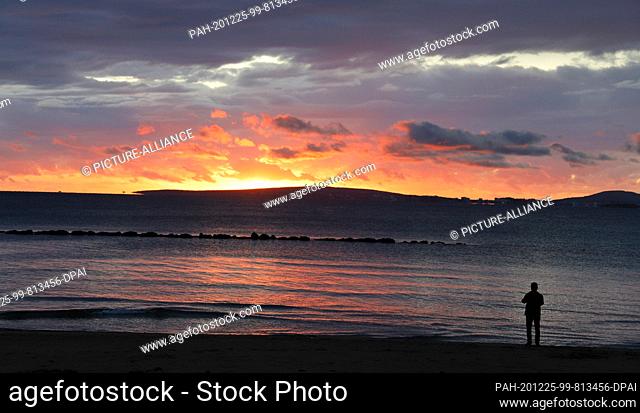 25 December 2020, Spain, Palma: A man watches the sunset on the beach of Palma on a rainy day. Cold and rain characterize the weather forecast in Mallorca for...