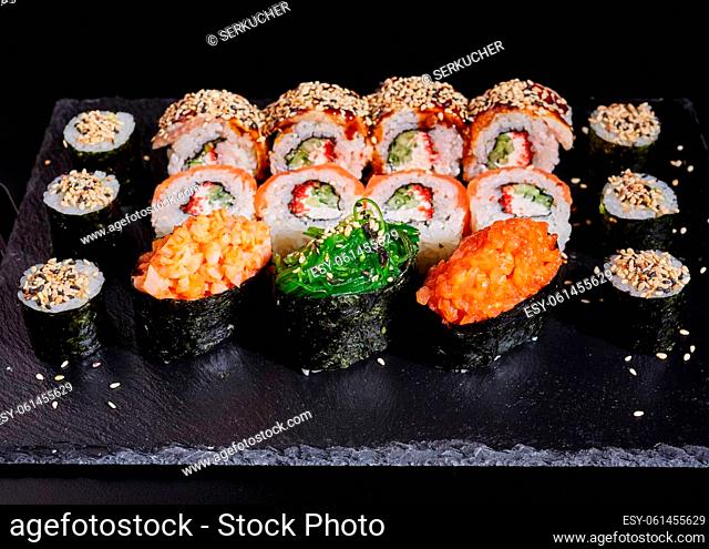Close up of a set of sushi on a black stone board on a dark table. Close up set of different sushi rolls sprinkled with sesame seeds on a black stone board on a...