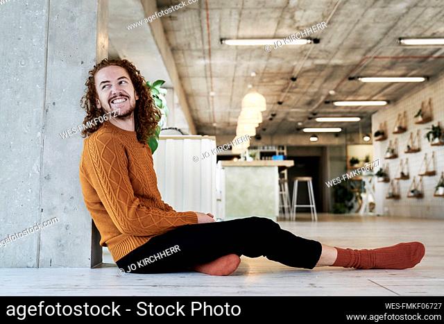 Smiling man looking away while sitting against architectural column in living room at home