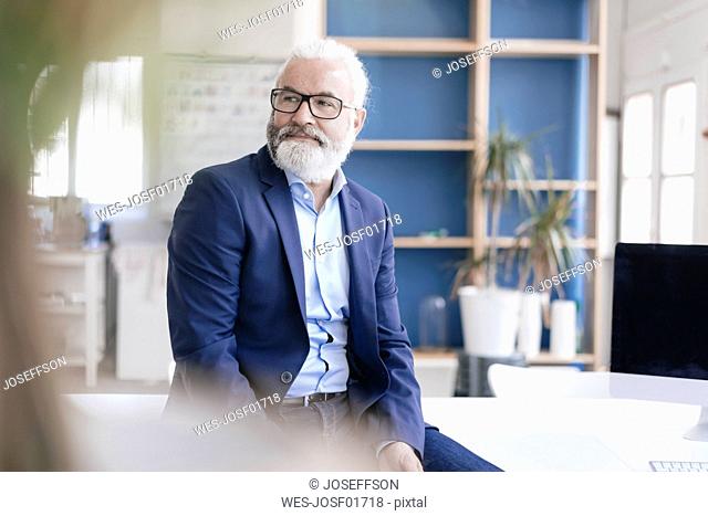 Confident mature man with beard and glasses in office