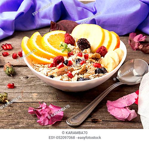 Healthy breakfast. Muesli with orange fruit, apple, pomegranate, nuts, banana and honey in white bowl over on old wooden table