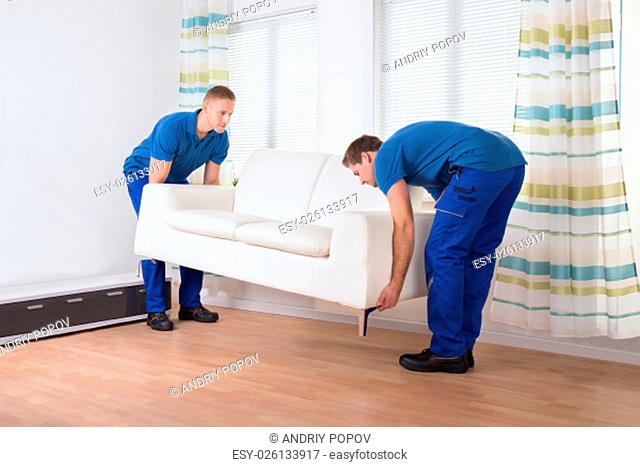 Full length of male movers placing sofa on hardwood floor at home
