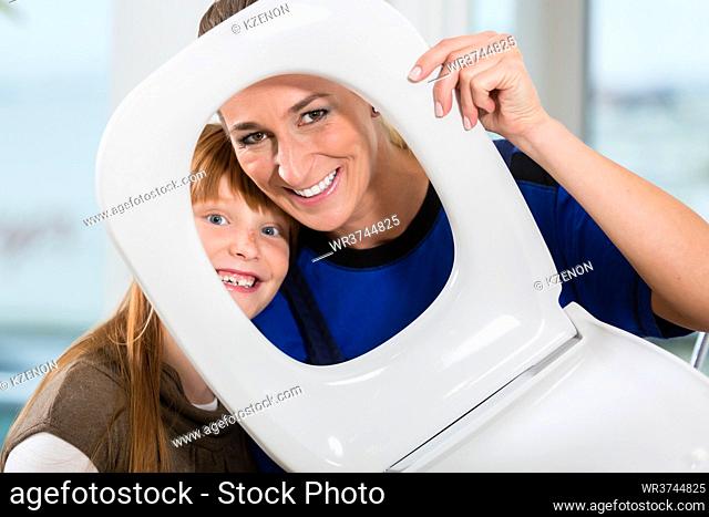 Funny portrait of a cheerful woman and her cute daughter smiling and looking at camera through a white toilet seat in a sanitary ware shop