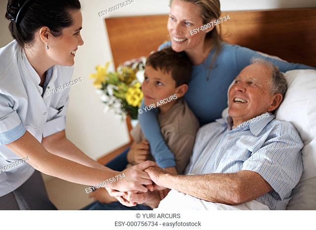 Doctor shaking hands with a recovered senior patient , family by the bed