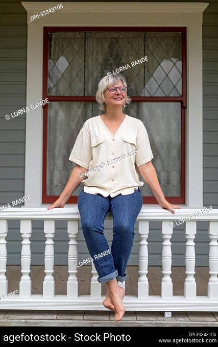 Portrait of a mature woman sitting on a railing in casual clothing; Surrey, British Columbia, Canada