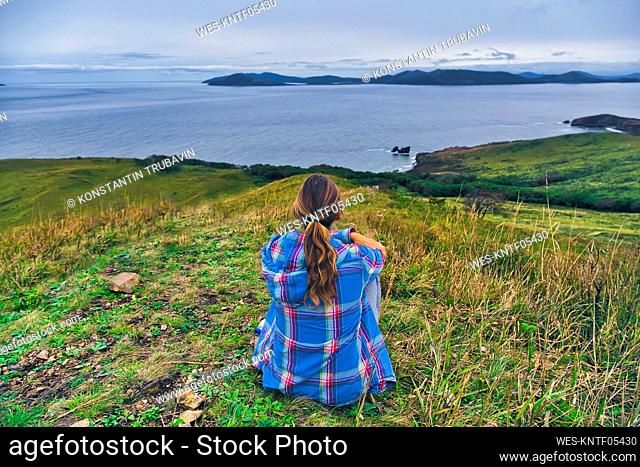 Woman looking at sea of Japan while sitting on mountain, Krabbe Peninsula, Primorsky Krai, Russia