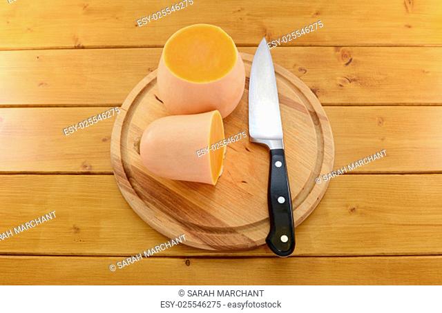 Butternut squash cut in half with a sharp kitchen knife on a wooden chopping board