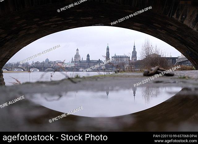 10 January 2022, Saxony, Dresden: The backdrop of the old town is reflected in a puddle under an arch of the Marienbrücke bridge on the banks of the Elbe