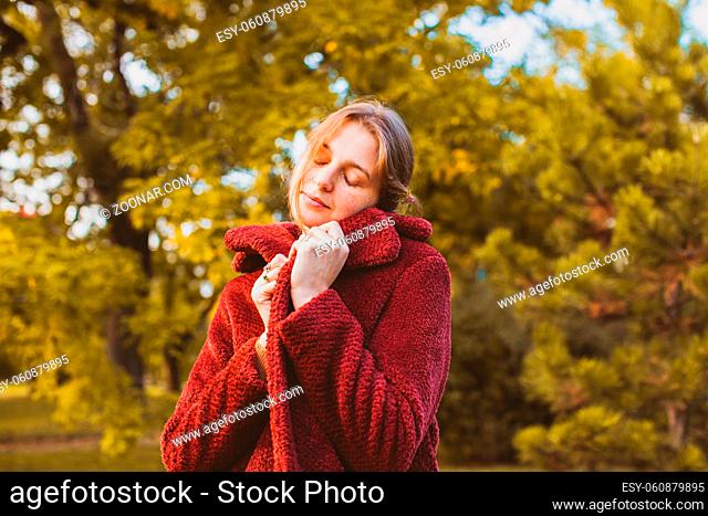 Portrait of young attractive woman wearing stylish soft cloth coat, wrapping herself up, feeling softness of the fabric. Beautiful girl in warm old-fashioned...