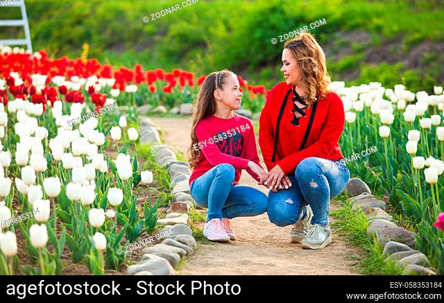 The mom with her daughter among a field of red and white tulips. They sit on the path and look at each other
