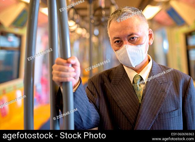 Portrait of mature Japanese businessman with mask for protection from corona virus outbreak at the sky train station