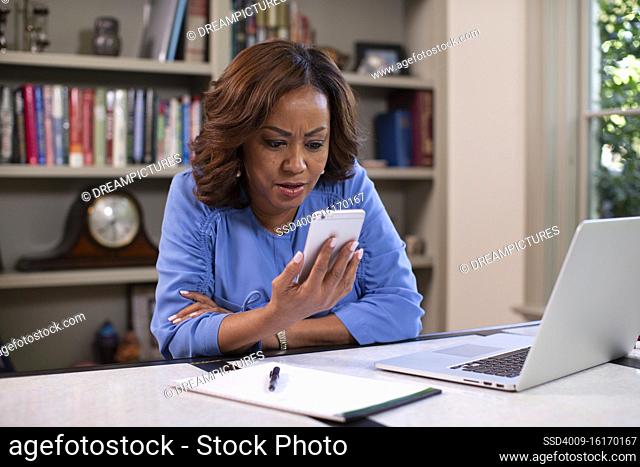 Middle aged black female doctor in home office providing telemedicine service, talking to patient on video call reacting to the patients situation