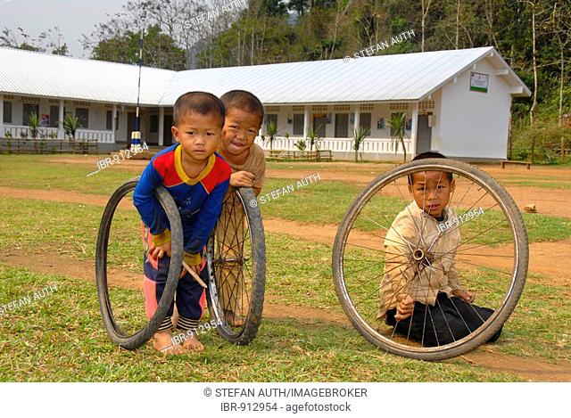 Children playing with old tyres in front of a school, Khmu People village near Luang Prabang, Laos, Southeast Asia