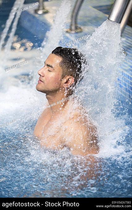 Vertical indoors shot of man with eyes closed refreshing under shower in pool