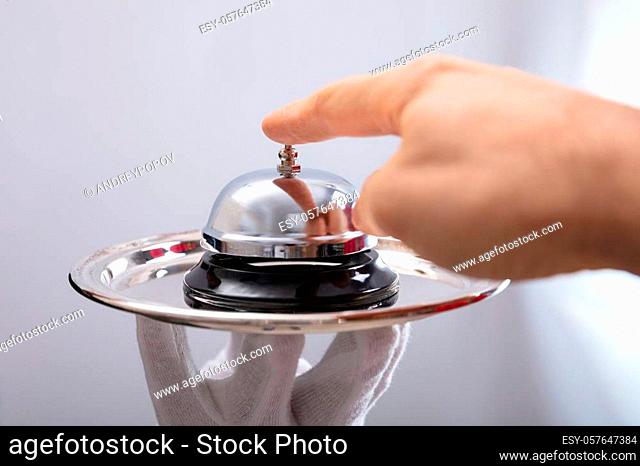 Close-up Of Person's Hand Ringing Service Bell On Plate Held By Waiter